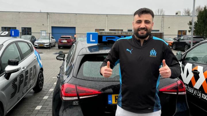 Geslaagde leerling van Rijles32 steekt twee duimen op bij de lesauto