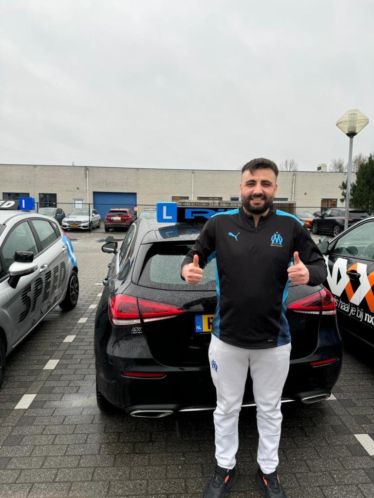 Geslaagde leerling van Rijles32 steekt twee duimen op bij de lesauto